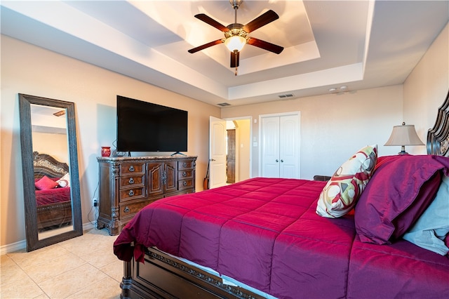 tiled bedroom featuring ceiling fan, a raised ceiling, and a closet