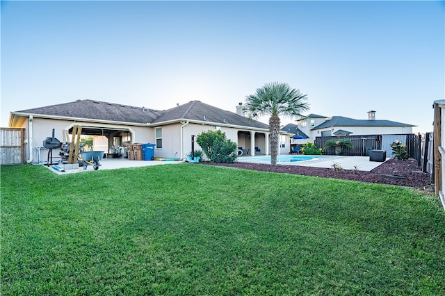 rear view of property featuring a lawn, a fenced in pool, and a patio area