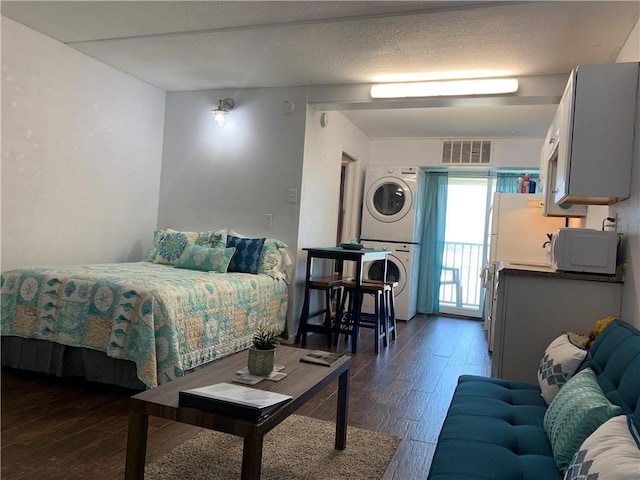 bedroom featuring dark hardwood / wood-style floors, a textured ceiling, and stacked washer / dryer