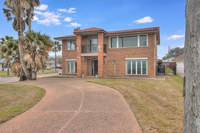 view of front of house with a front yard, a balcony, a gate, a chimney, and brick siding