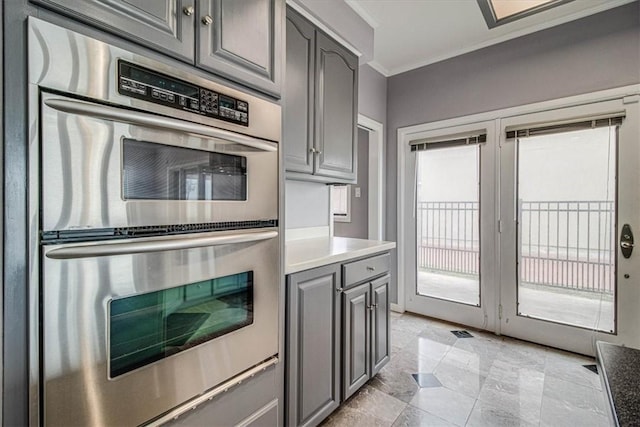 kitchen featuring stainless steel double oven, ornamental molding, gray cabinets, and light countertops