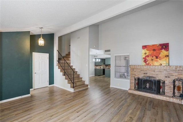 unfurnished living room with wood-type flooring, a brick fireplace, a towering ceiling, and a textured ceiling