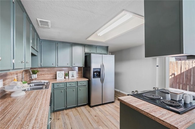 kitchen featuring sink, stainless steel fridge, black electric stovetop, a textured ceiling, and light wood-type flooring