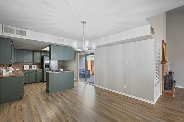 kitchen featuring dark hardwood / wood-style floors, decorative light fixtures, stainless steel refrigerator with ice dispenser, a brick fireplace, and an inviting chandelier