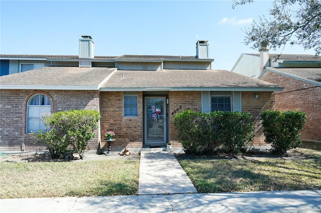 view of front of property with a front yard, brick siding, roof with shingles, and a chimney