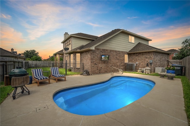 pool at dusk featuring central air condition unit and a patio area