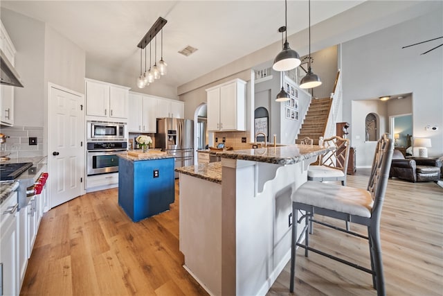 kitchen with white cabinets, tasteful backsplash, a kitchen island, appliances with stainless steel finishes, and decorative light fixtures