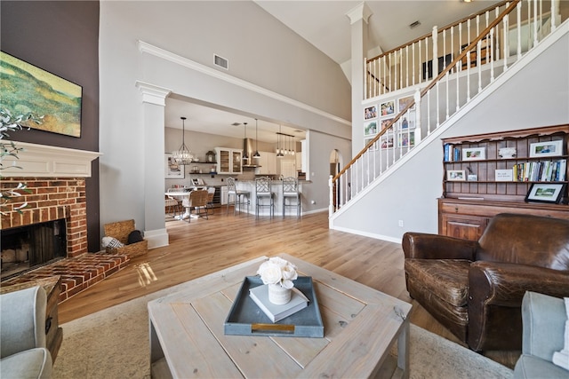 living room with a brick fireplace, wood-type flooring, an inviting chandelier, and high vaulted ceiling