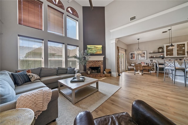 living room featuring a brick fireplace, a towering ceiling, a notable chandelier, and light wood-type flooring