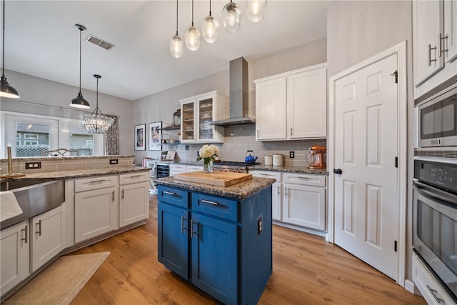 kitchen featuring light hardwood / wood-style floors, hanging light fixtures, wall chimney range hood, a kitchen island, and white cabinetry