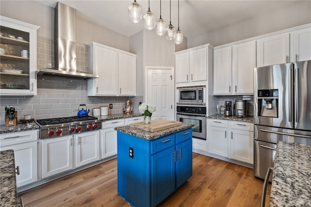 kitchen with light stone counters, appliances with stainless steel finishes, wall chimney exhaust hood, a center island, and blue cabinets