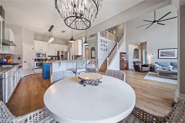 dining space with ceiling fan with notable chandelier, light hardwood / wood-style flooring, and a high ceiling