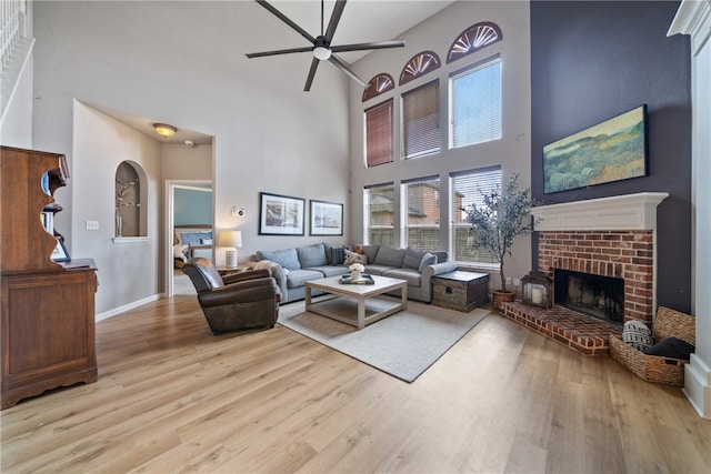 living room with a high ceiling, ceiling fan, a brick fireplace, and light hardwood / wood-style flooring