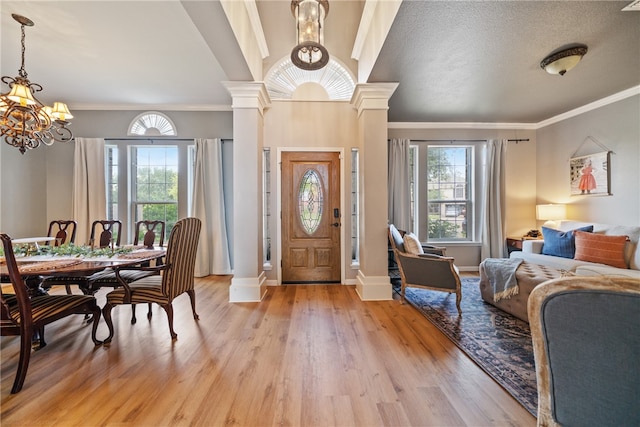 foyer with crown molding, a textured ceiling, an inviting chandelier, decorative columns, and light hardwood / wood-style flooring