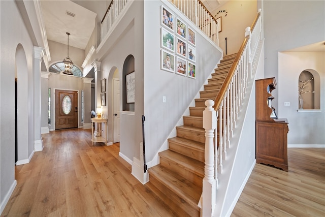 entrance foyer featuring ornate columns, an inviting chandelier, light hardwood / wood-style floors, and a towering ceiling