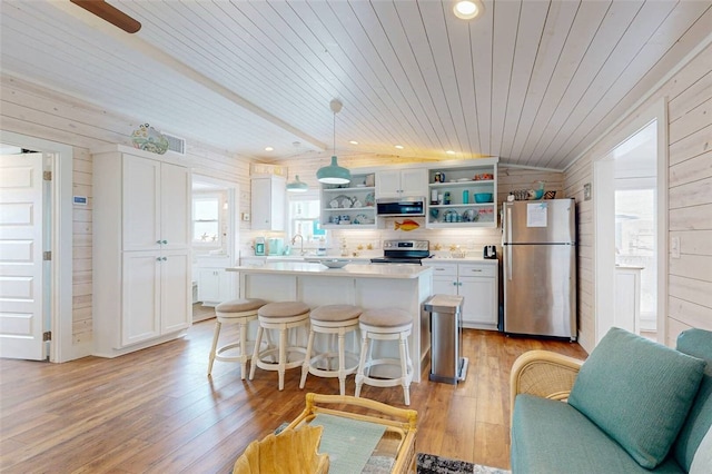 kitchen with hanging light fixtures, wood walls, stainless steel appliances, and plenty of natural light