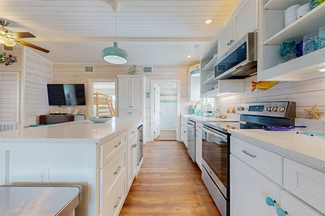 kitchen with white cabinets, decorative light fixtures, stainless steel appliances, and wood walls