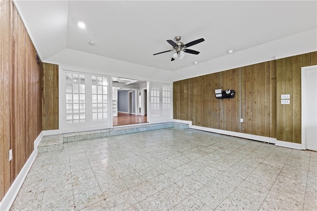 unfurnished living room featuring wood walls, french doors, vaulted ceiling, and ceiling fan