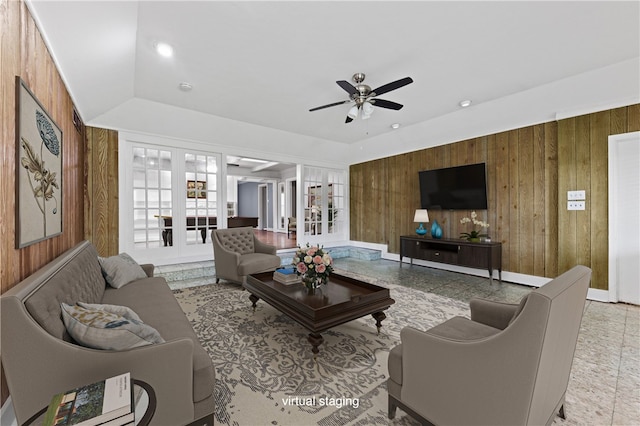 living room with french doors, wooden walls, ceiling fan, and vaulted ceiling