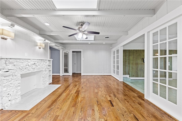 unfurnished living room featuring a stone fireplace, french doors, hardwood / wood-style flooring, and beam ceiling