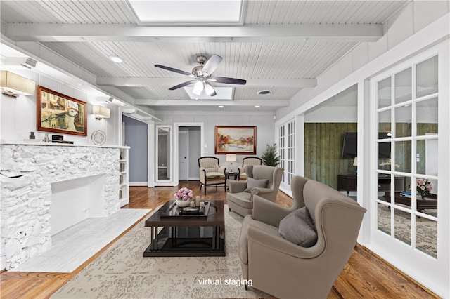 living room featuring wood-type flooring, french doors, a stone fireplace, beamed ceiling, and ceiling fan