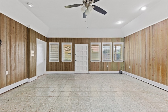 empty room featuring wood walls, vaulted ceiling, and ceiling fan