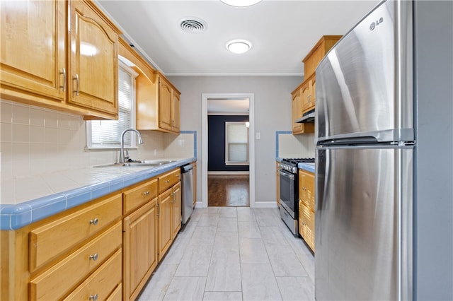 kitchen featuring stainless steel appliances, tile countertops, sink, ornamental molding, and backsplash