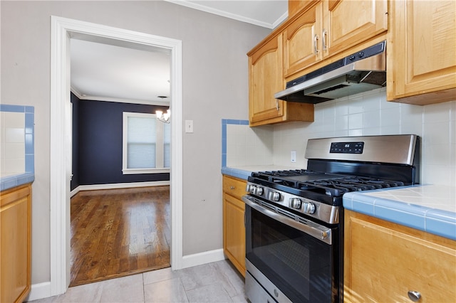 kitchen with stainless steel gas range, tile counters, light hardwood / wood-style floors, and crown molding