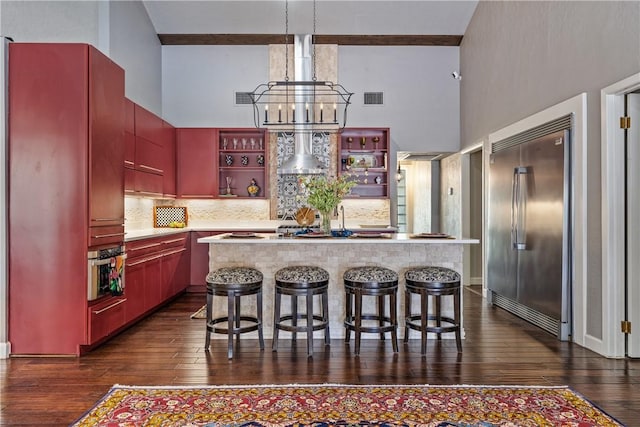 kitchen featuring wall chimney exhaust hood, a towering ceiling, backsplash, and appliances with stainless steel finishes