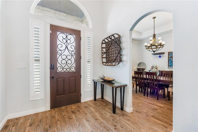 foyer with a tray ceiling, light wood-style flooring, baseboards, and an inviting chandelier