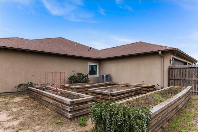 back of property with a garden, fence, central AC unit, and stucco siding