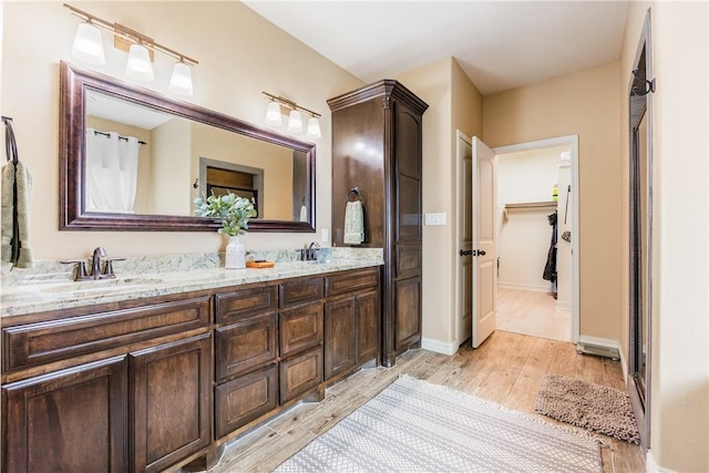 full bath with double vanity, wood finished floors, a sink, and baseboards