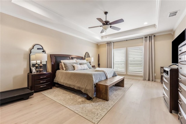 bedroom with visible vents, a tray ceiling, and light wood-style flooring