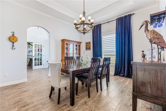 dining area with light wood-style floors, arched walkways, a raised ceiling, and crown molding