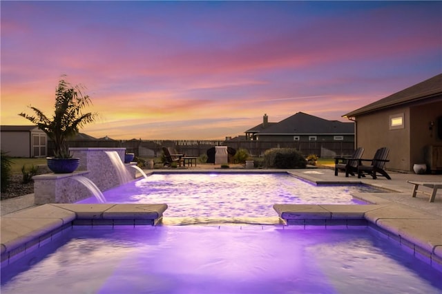 pool at dusk featuring a patio, a fenced backyard, an outdoor structure, a fenced in pool, and a storage unit