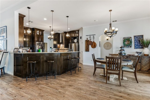 kitchen with a chandelier, dark brown cabinets, wall chimney range hood, and light countertops