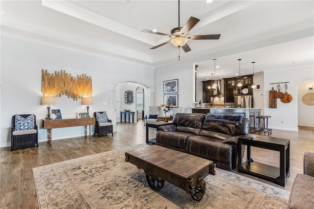 living area featuring arched walkways, baseboards, a tray ceiling, and wood finished floors