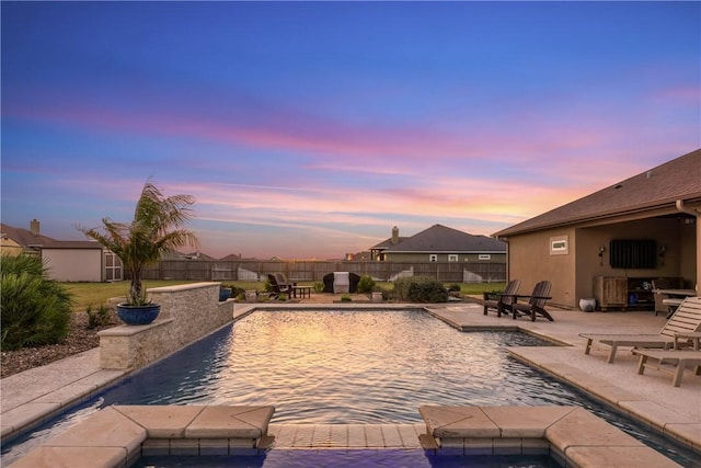 pool at dusk featuring an outbuilding, a patio, a storage unit, and a fenced backyard