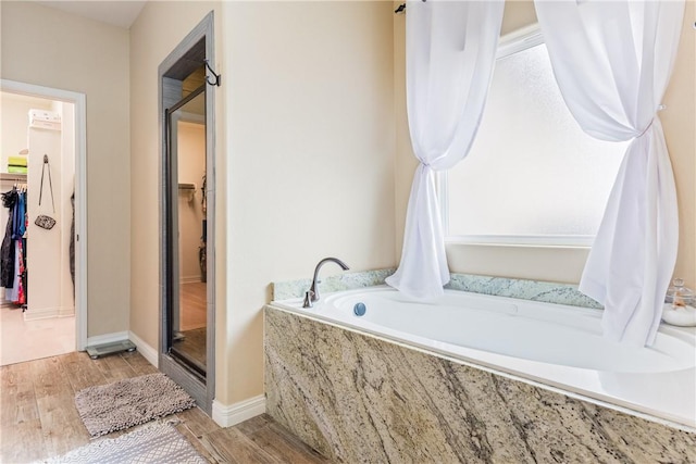 full bathroom featuring a walk in closet, a bath, and wood finished floors