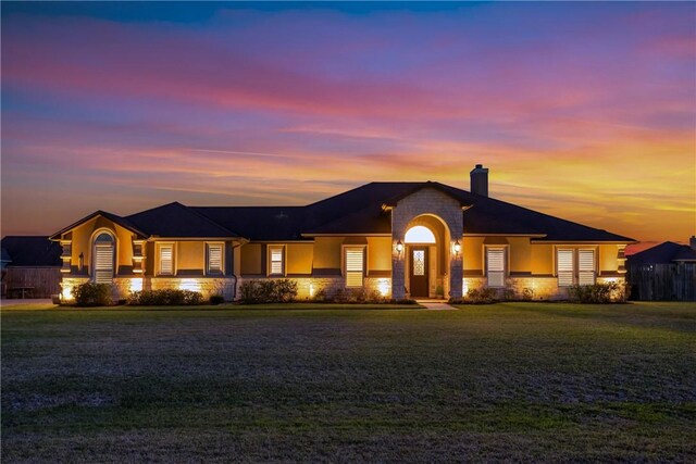 view of front of house featuring stone siding, a chimney, a front lawn, and stucco siding