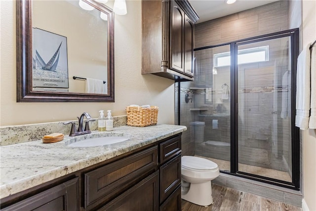 bathroom with a stall shower, vanity, toilet, and wood finished floors