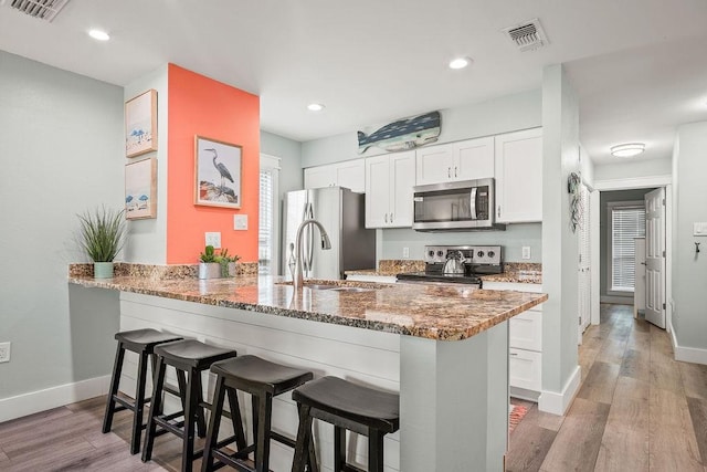 kitchen featuring stainless steel appliances, stone countertops, visible vents, and a kitchen breakfast bar