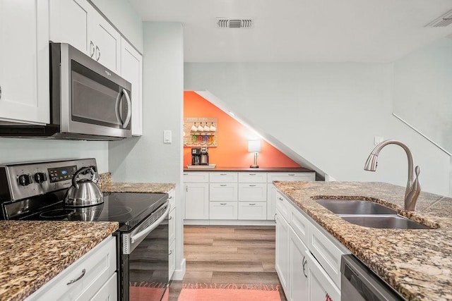 kitchen with a sink, visible vents, white cabinets, light wood-style floors, and appliances with stainless steel finishes