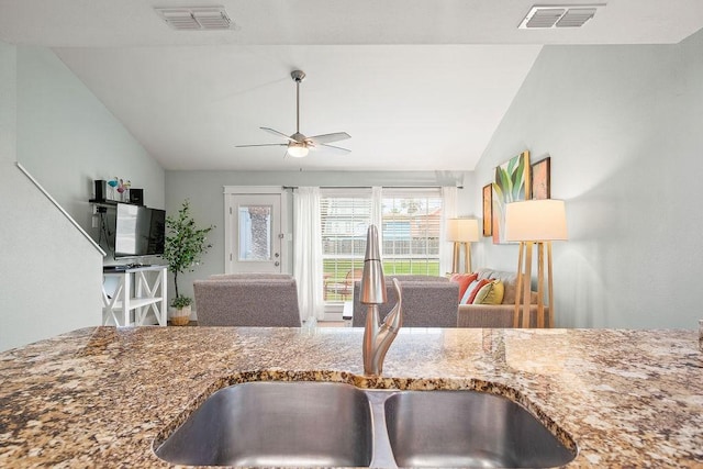 kitchen featuring vaulted ceiling, stone counters, a sink, and visible vents