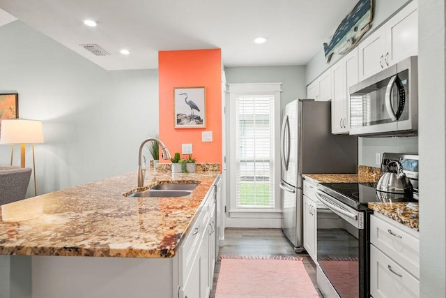 kitchen with light stone counters, stainless steel appliances, visible vents, a sink, and a peninsula