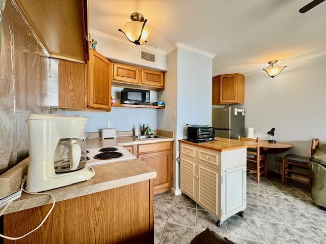 kitchen with wood counters, sink, light tile patterned floors, stainless steel refrigerator, and ornamental molding