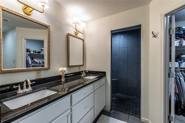 full bath with tiled shower, a sink, visible vents, and double vanity