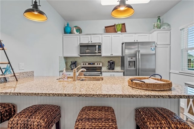 kitchen with appliances with stainless steel finishes, a kitchen bar, decorative backsplash, white cabinets, and kitchen peninsula