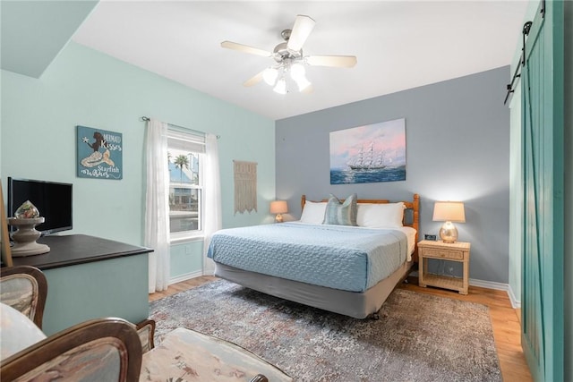 bedroom featuring a barn door, ceiling fan, and light wood-type flooring