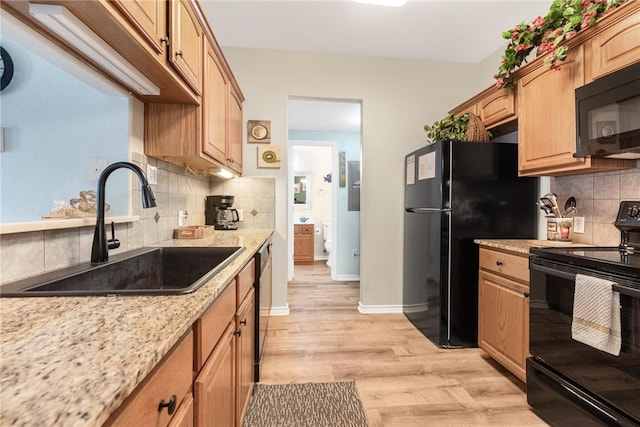 kitchen featuring sink, black appliances, light wood-type flooring, light stone countertops, and backsplash